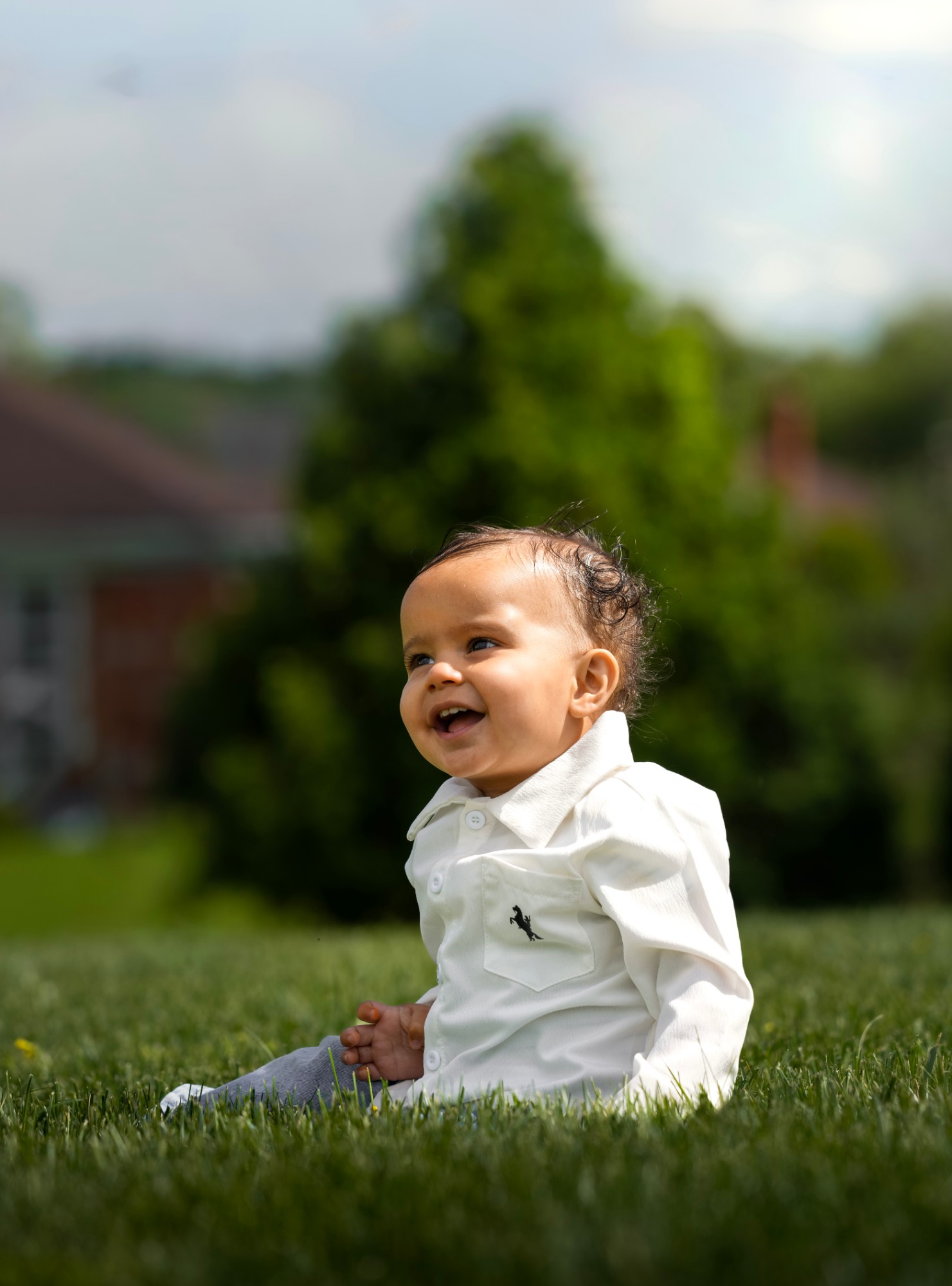 A laughing baby in a white shirt sitting on the grass
