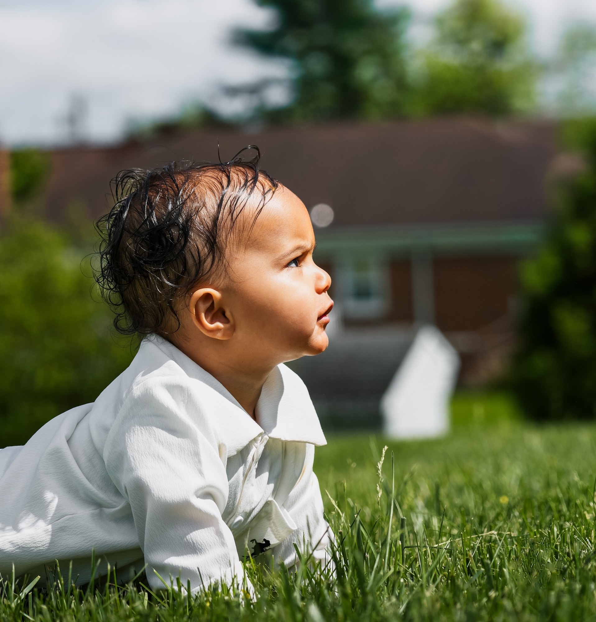 A baby in a white shirt lying on the grass, looking up and away