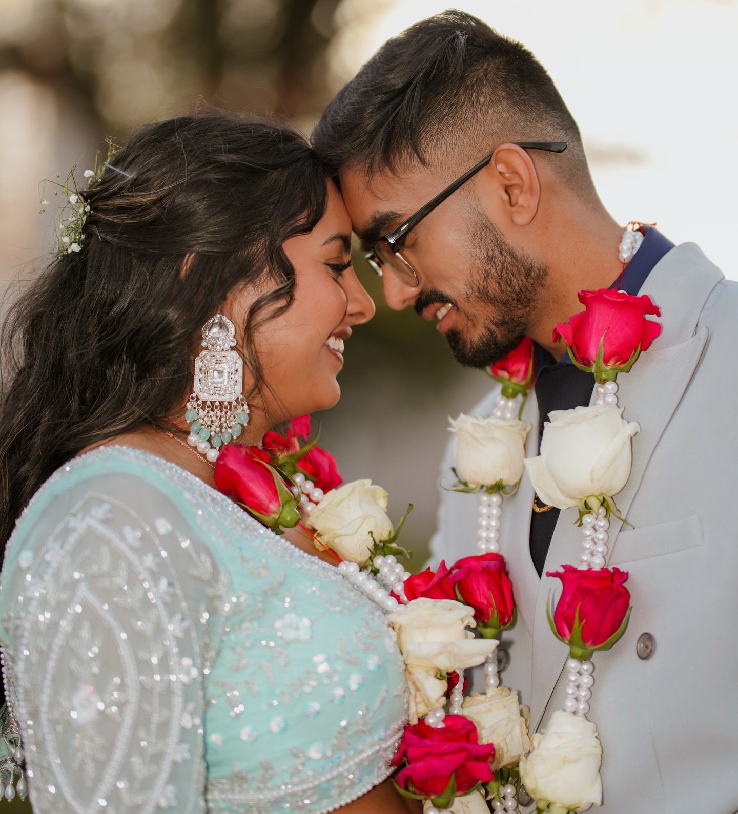 A couple wearing rose garlands touching foreheads and smiling