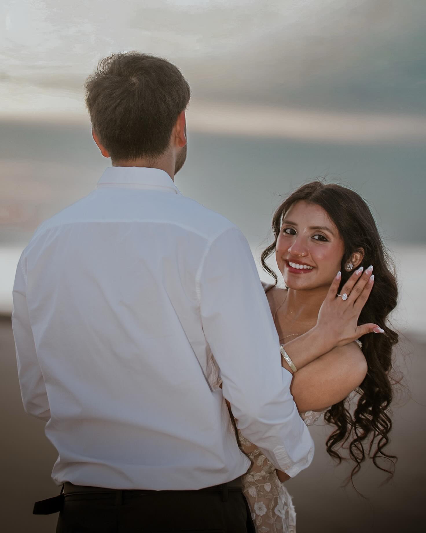 A woman smiling at the camera over her partner's shoulder, her engagement ring on show