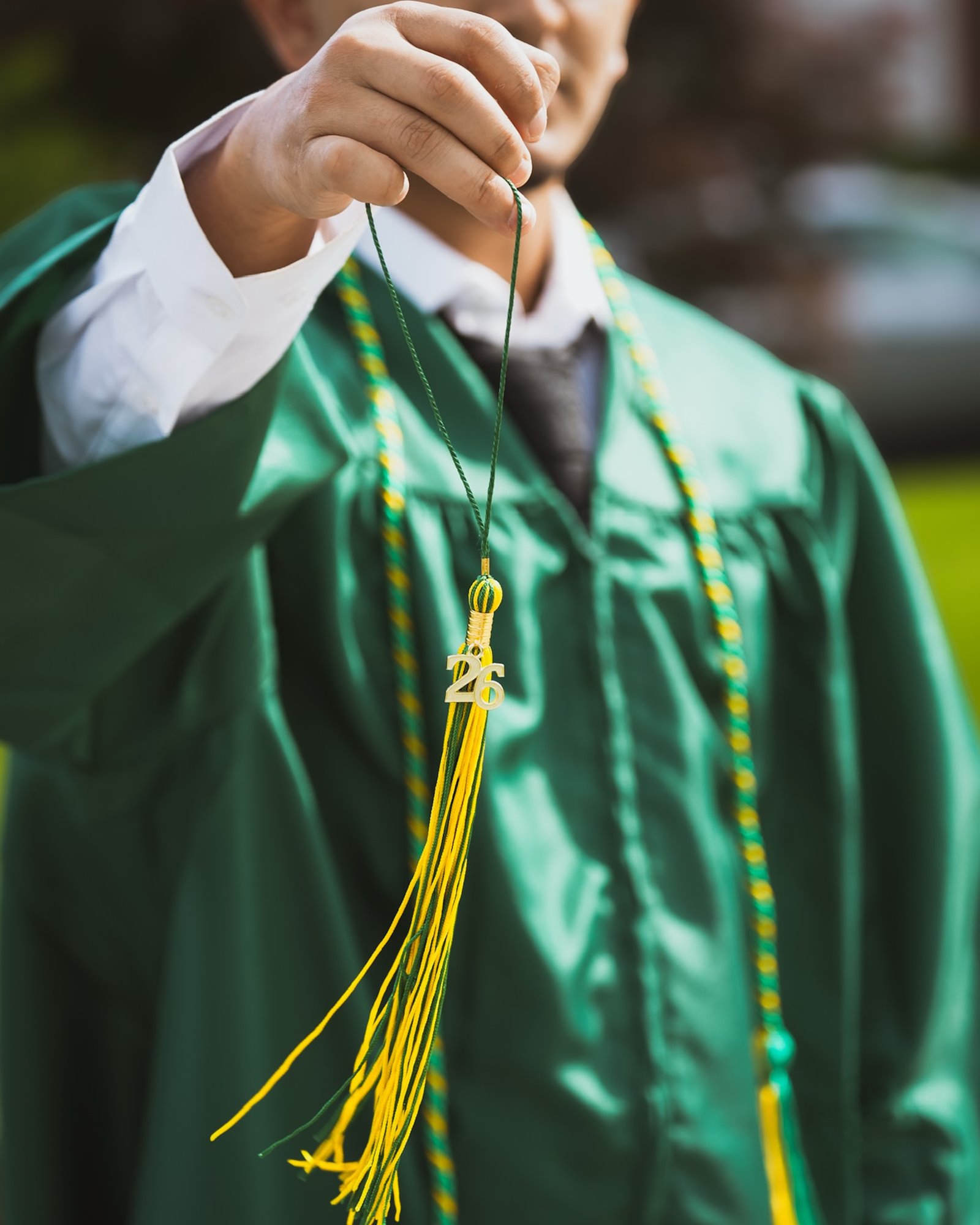 A graduate in a green gown holding up the gold tassel