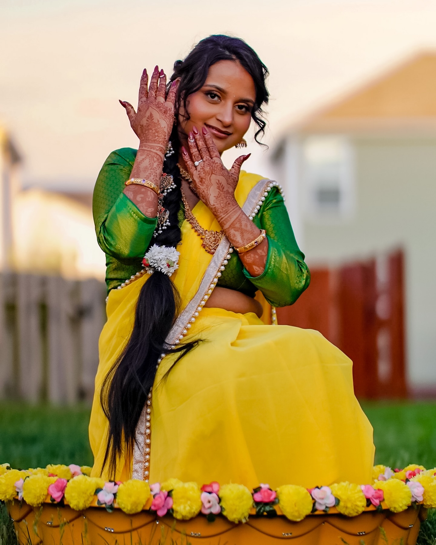 A woman in a yellow saree showing her mehendi-covered hands at her haldi ceremony