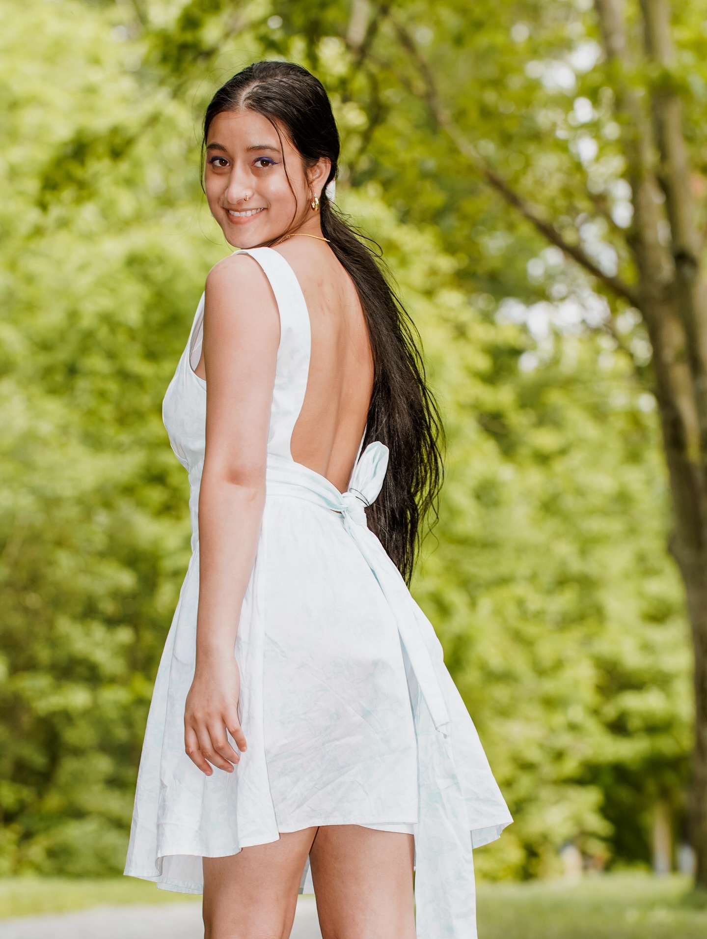 A woman in a white backless dress looking back over her shoulder, trees behind her