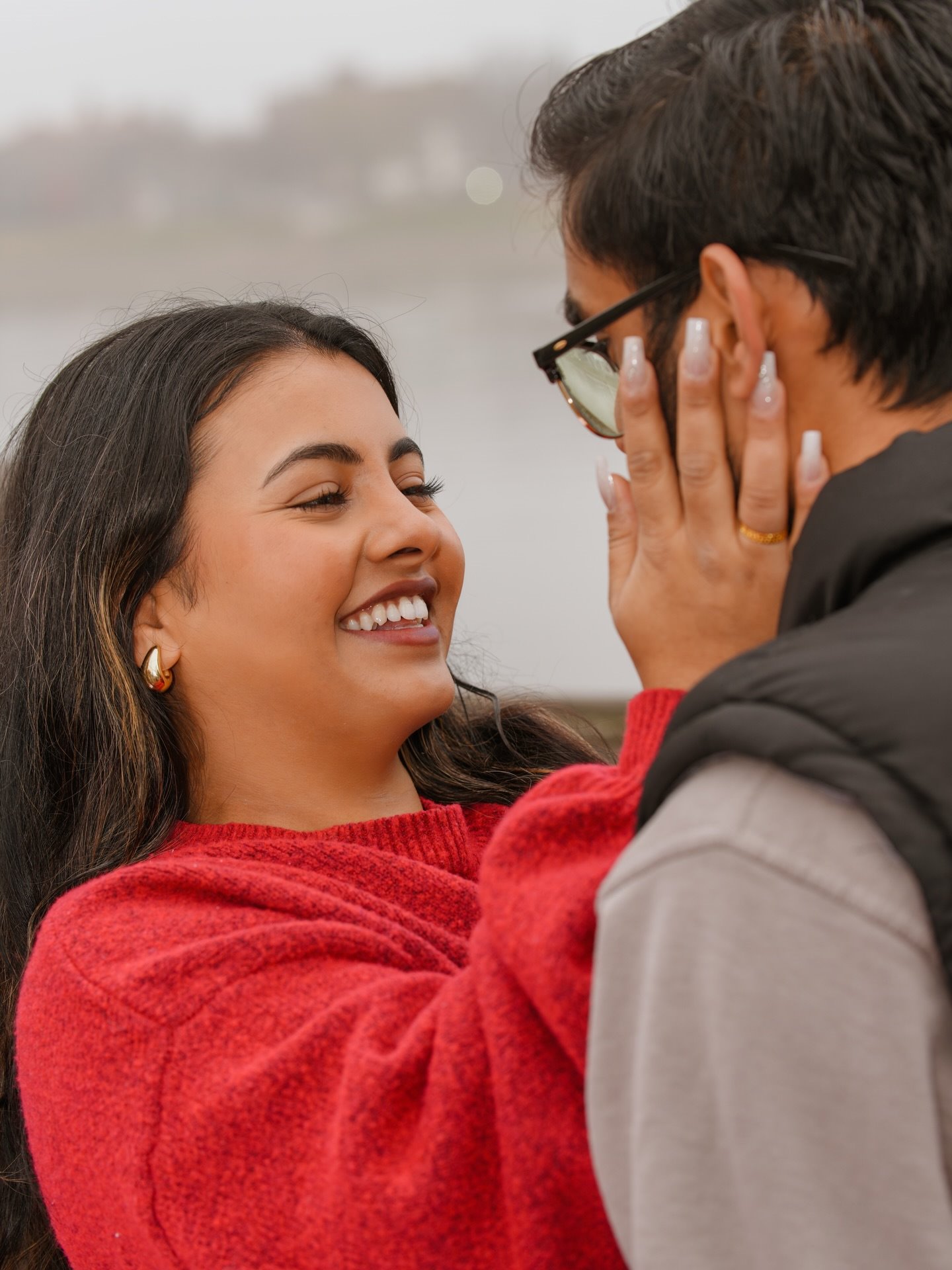 A woman in a red sweater laughing with her hand on her partner's cheek